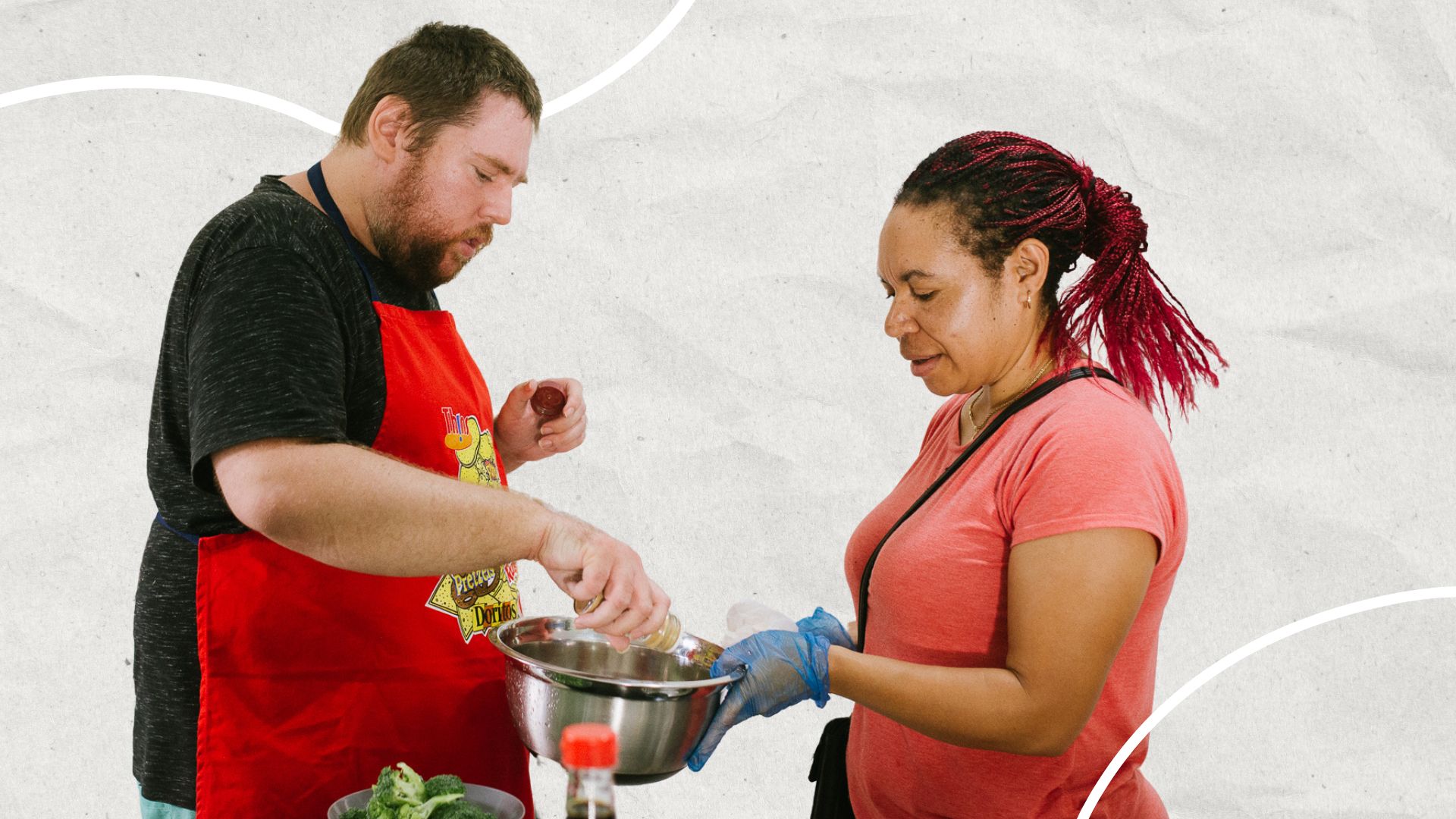 A man pours from a spice bottle into a bowl that a Support Worker is holding