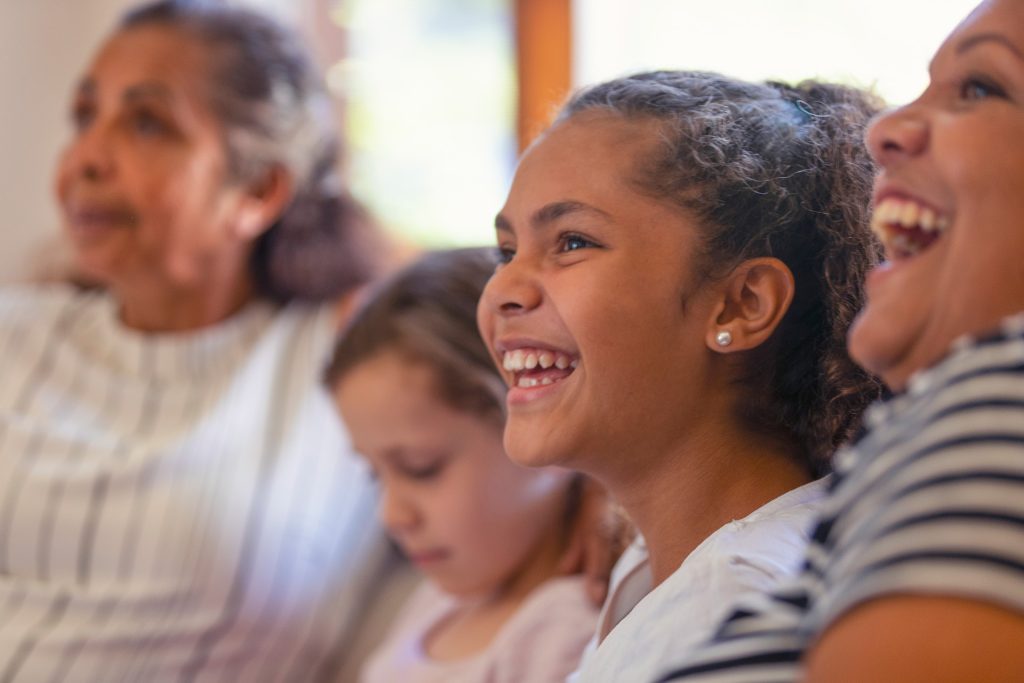 A girl laughs. She sits next to another girl and two women who are out of focus.